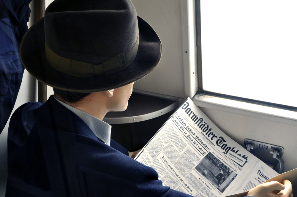Schaufensterpuppe sitzt in Zugabteil und liest das Darmstaedter Tagblatt